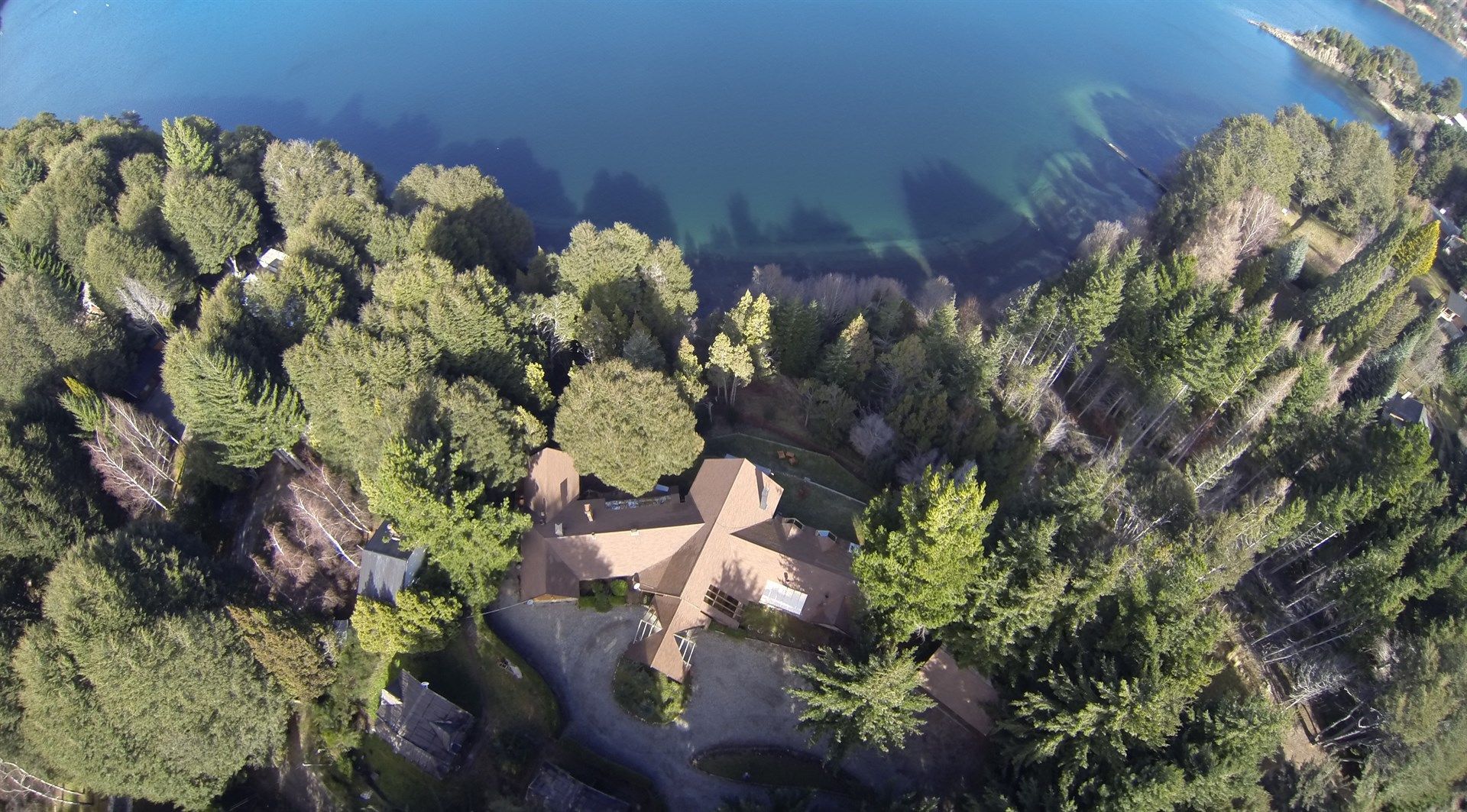 Una vista aérea de una casa rodeada de árboles junto a un cuerpo de agua.