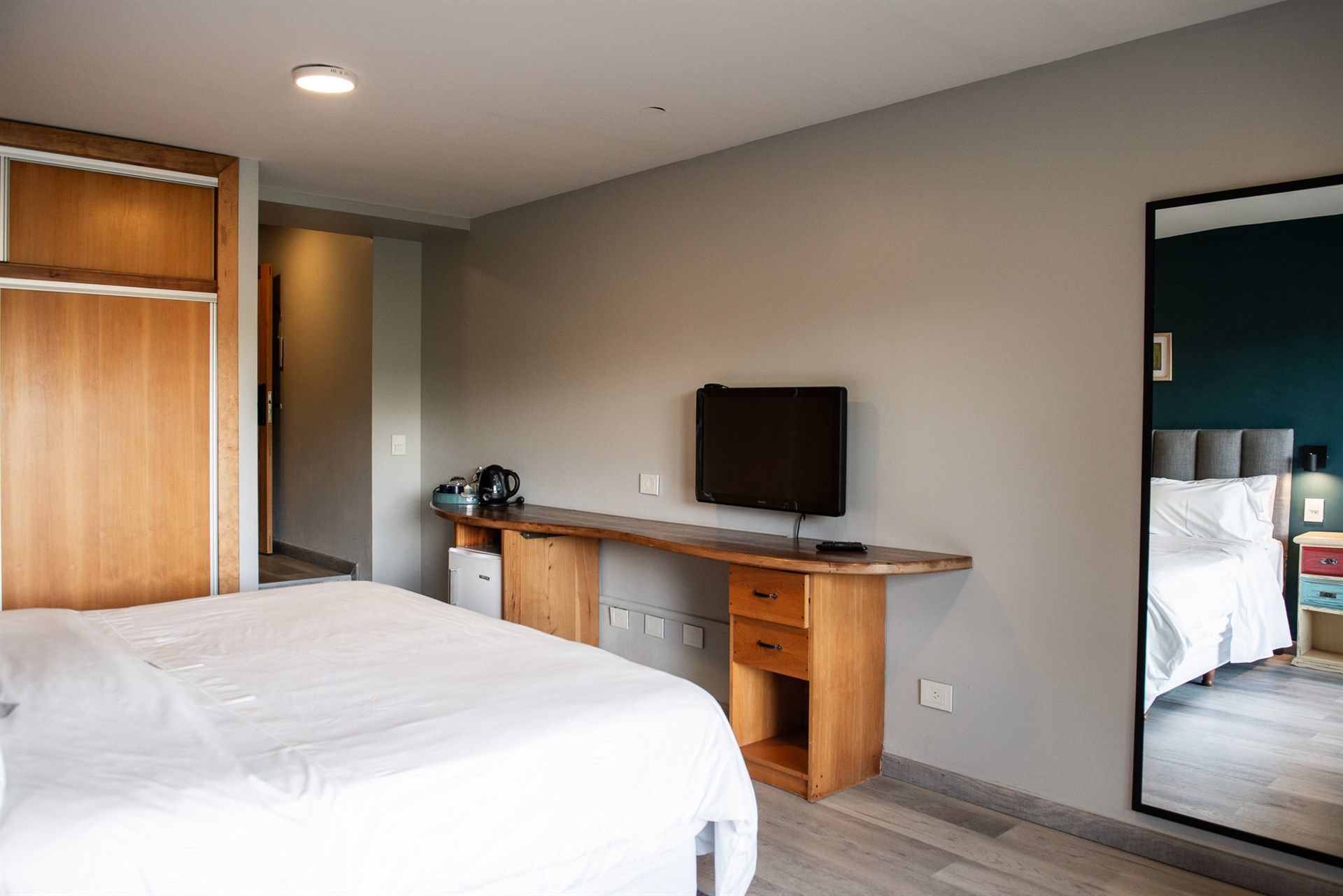 Una habitación de hotel con cama, escritorio, televisión y espejo.