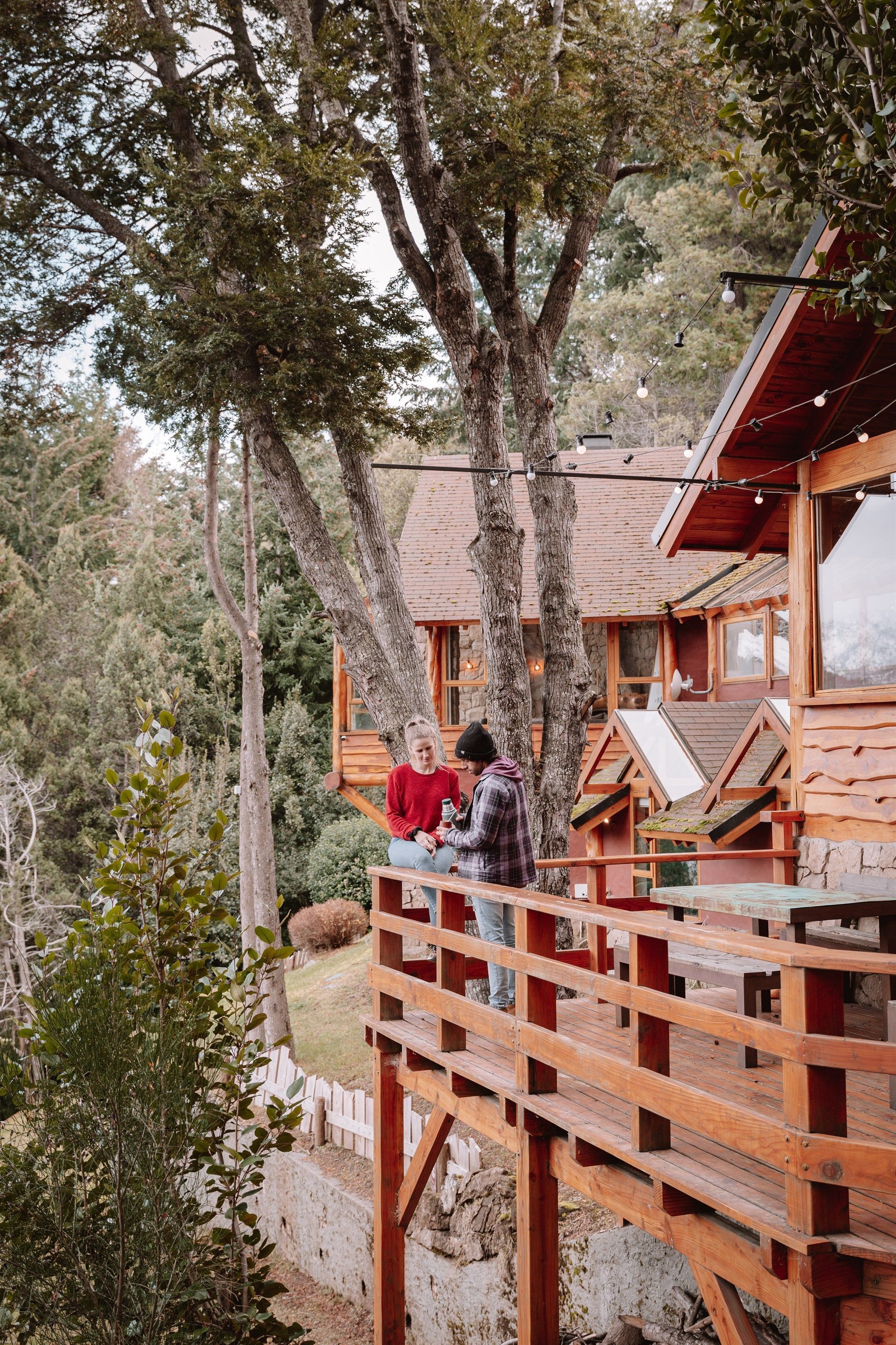 Un hombre y una mujer están sentados en una terraza de madera frente a una casa en el árbol.
