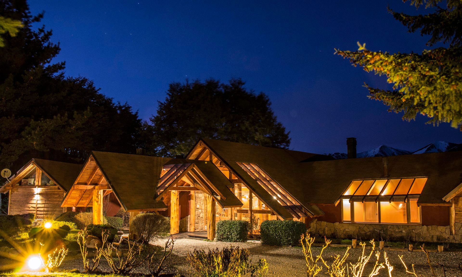 Una gran casa de madera está iluminada por la noche rodeada de árboles.