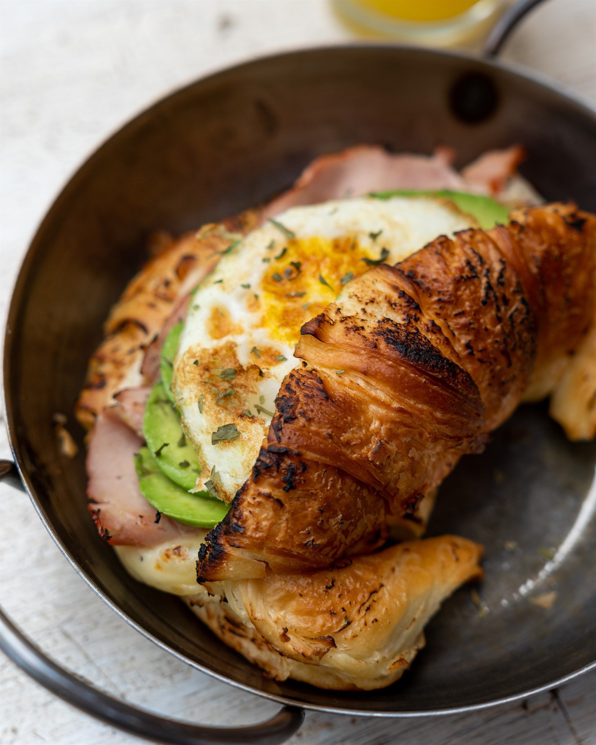 Un croissant con jamón, huevos y aguacate encima.