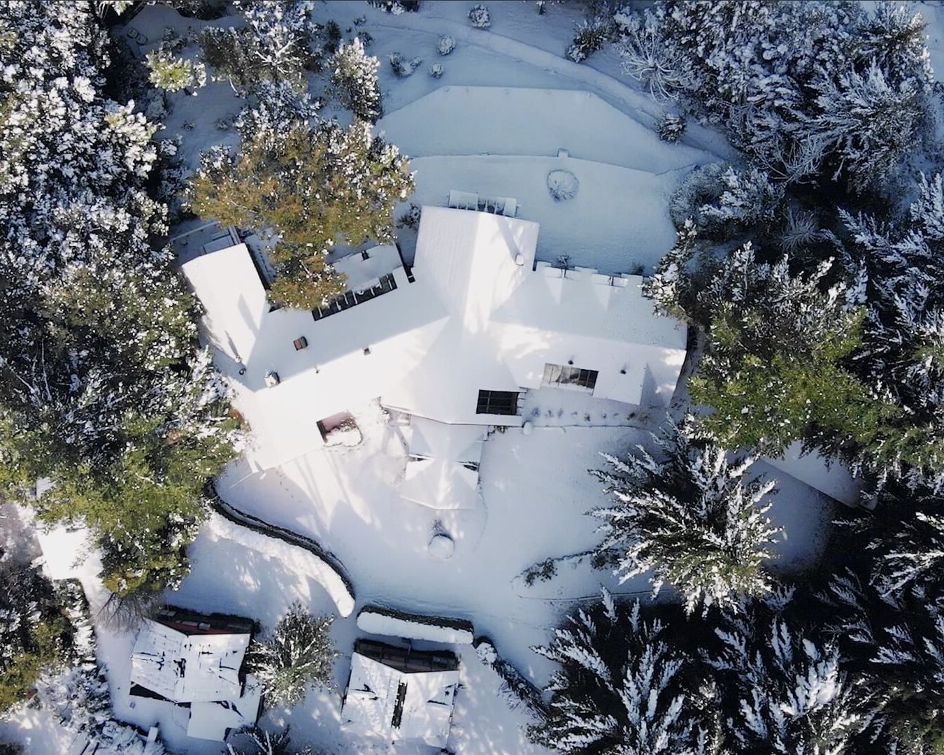 Una vista aérea de una casa rodeada de árboles cubiertos de nieve.