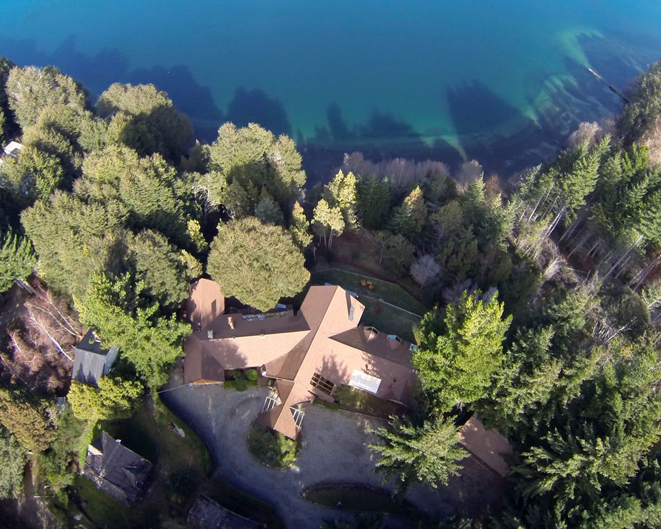 Una vista aérea de una casa rodeada de árboles junto a un cuerpo de agua.