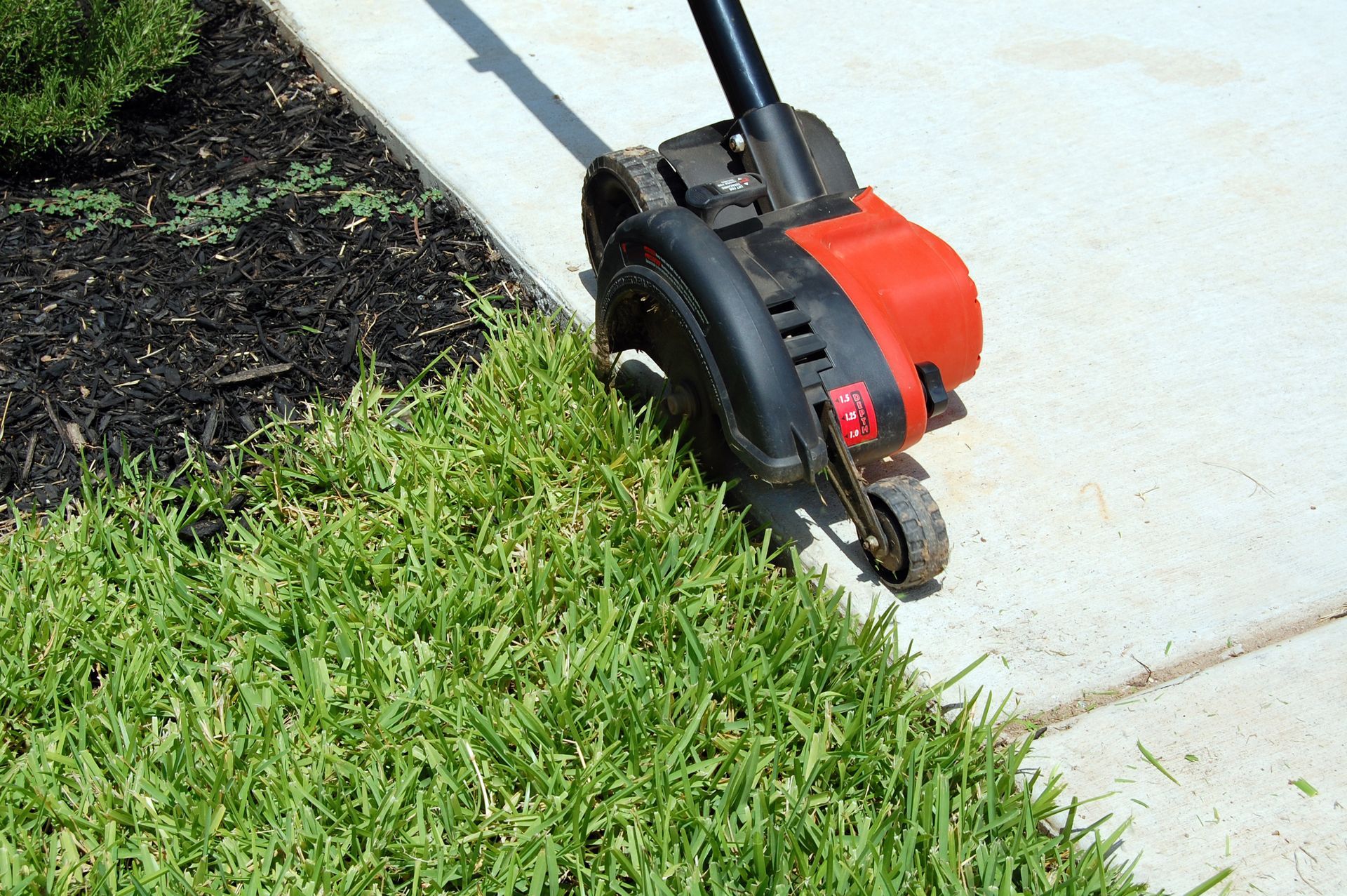 A lawn mower is cutting the grass on the sidewalk