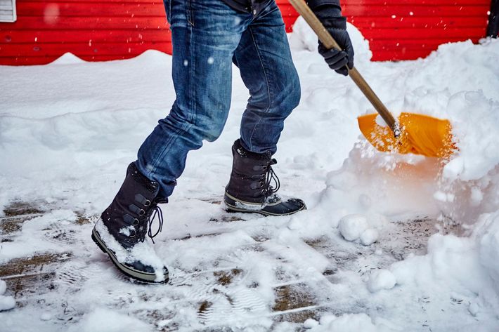 A person is shoveling snow from a sidewalk with a shovel.