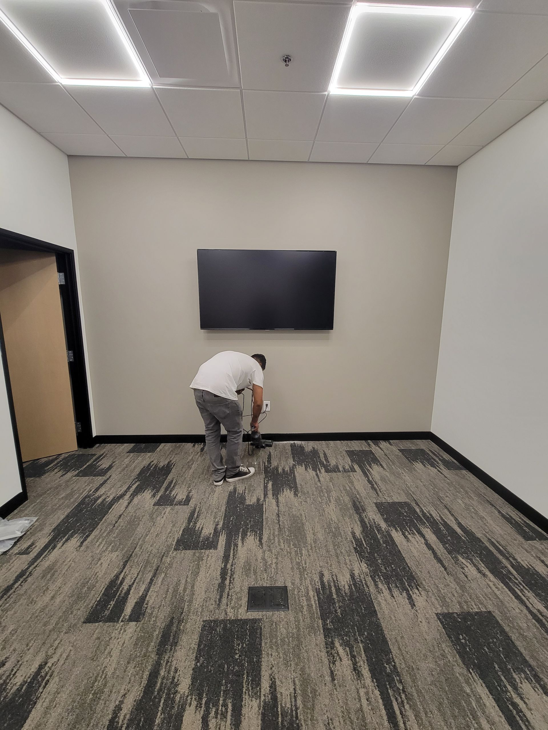 A man is bending over in a room with a flat screen tv on the wall.
