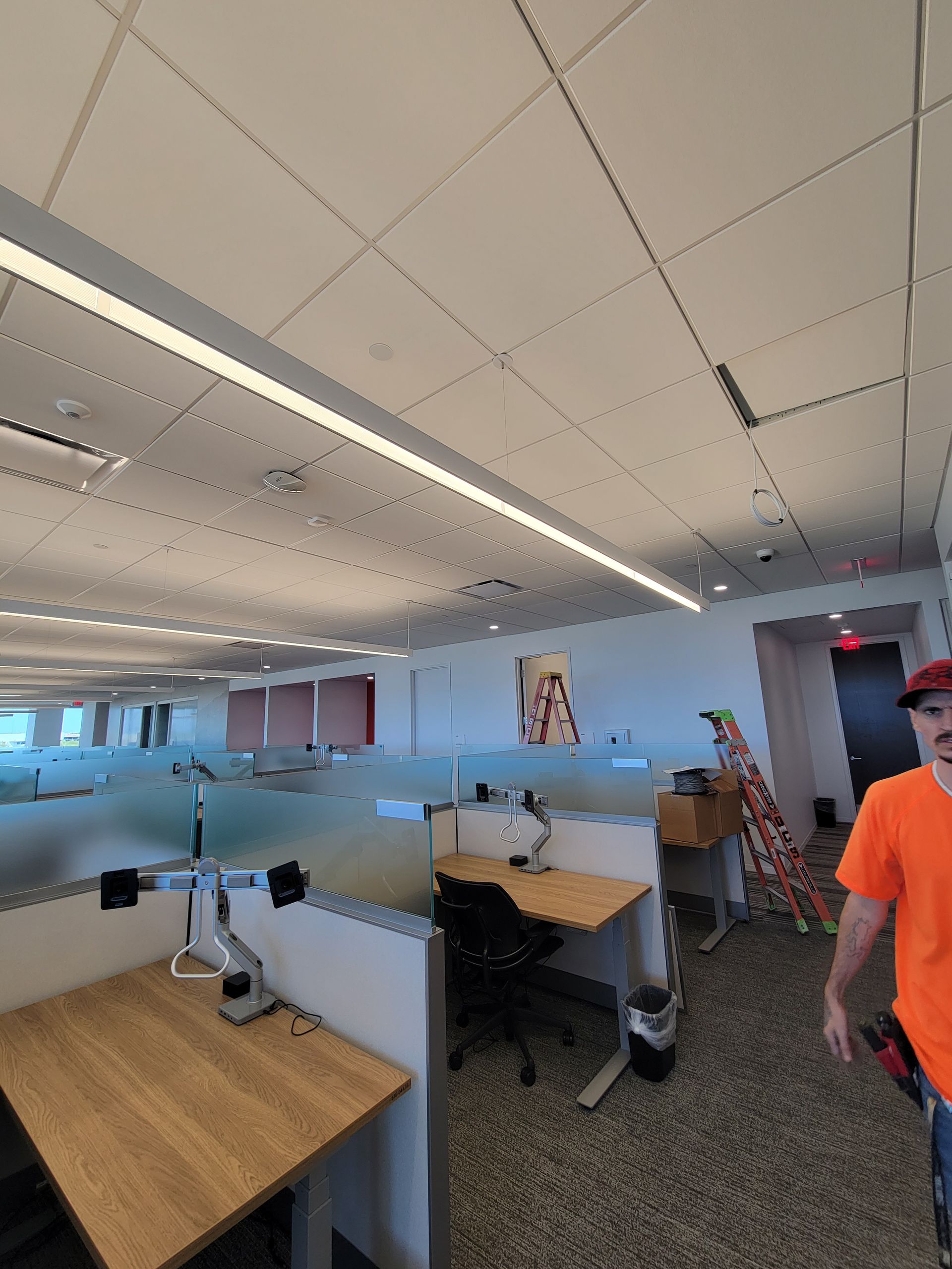 A man is walking through an office with cubicles and a ladder.