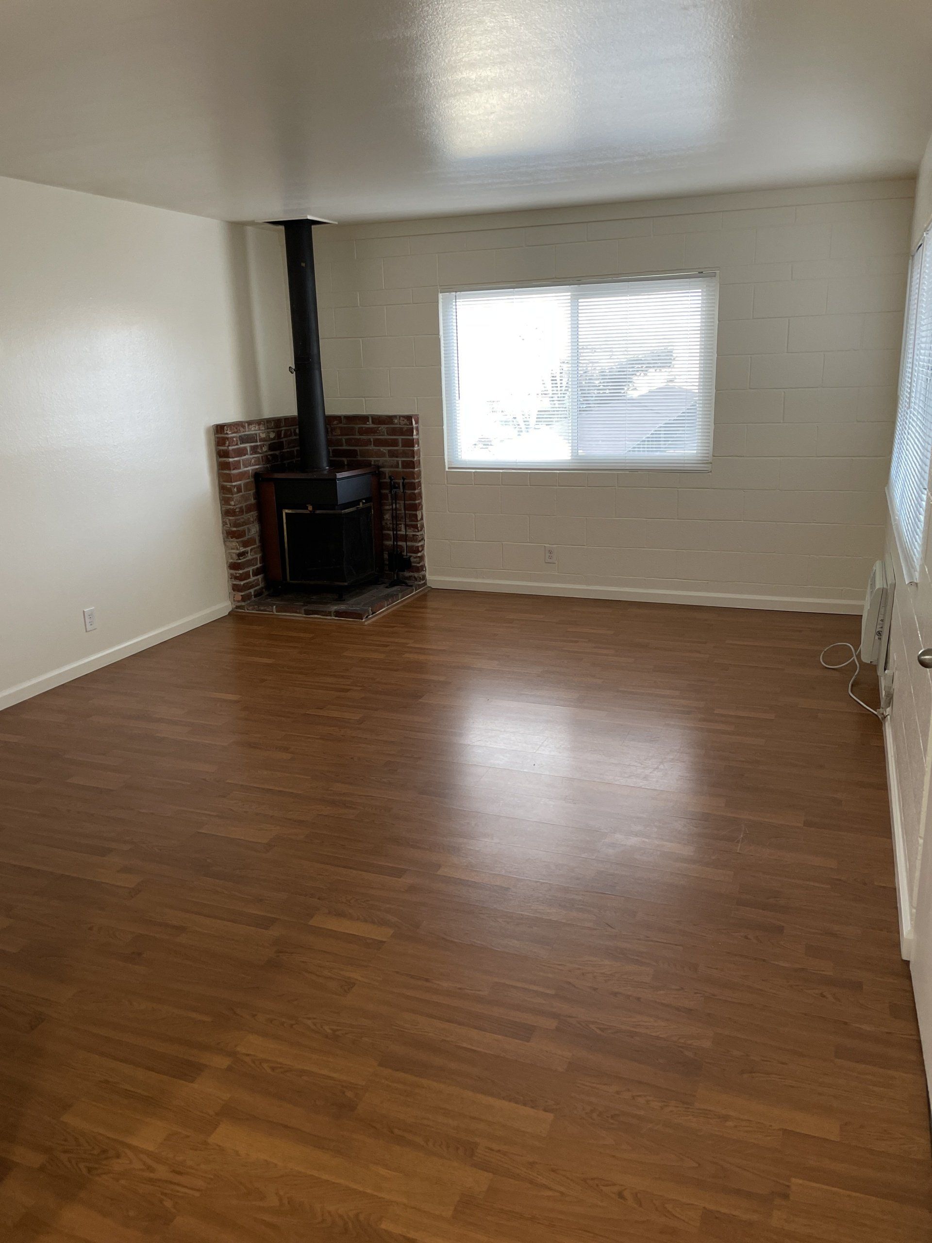 Interior view of River Arms Apartments living room with corner fireplace, wood flooring, and window.