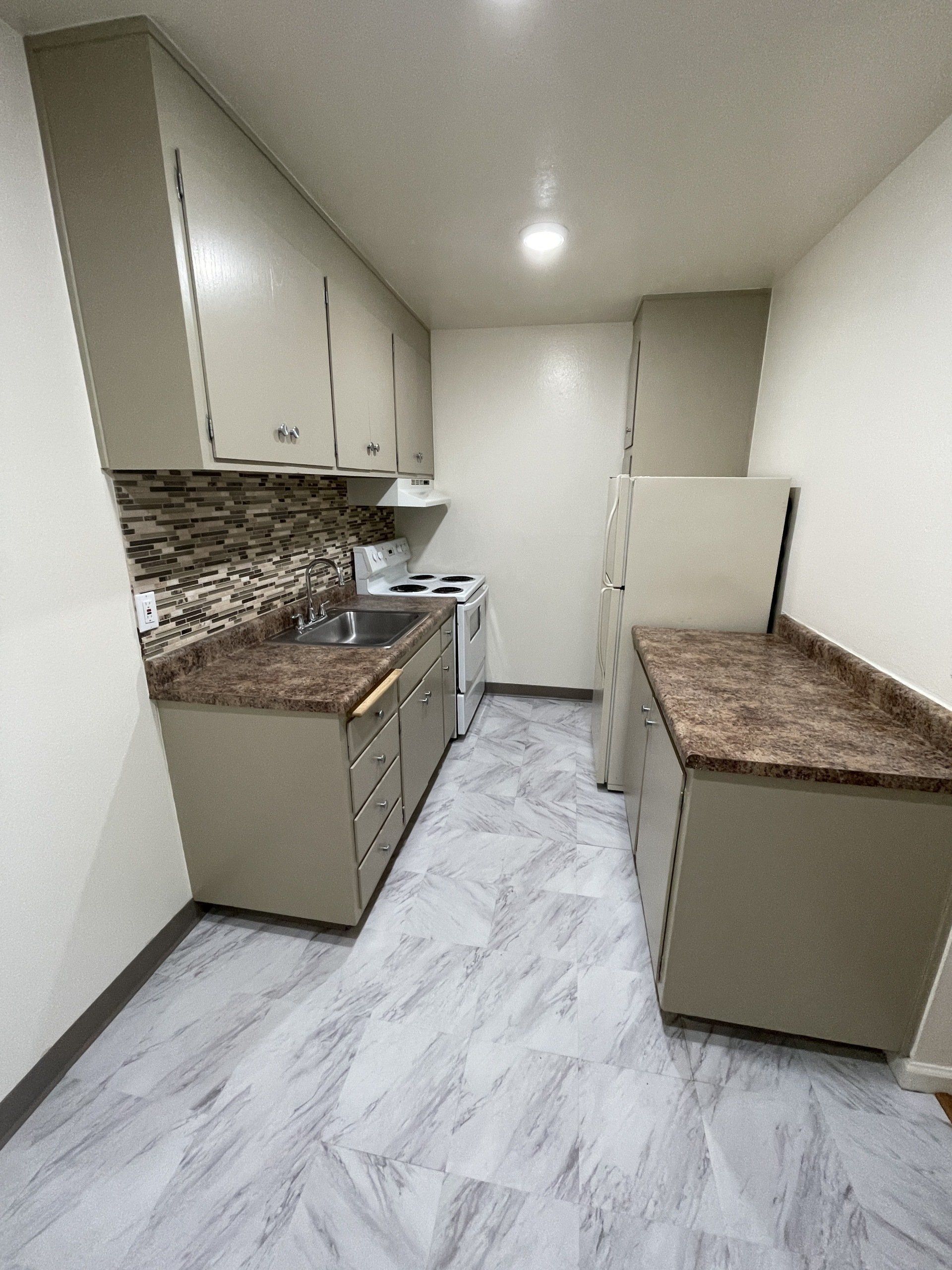 Interior view of River Arms Apartments kitchen with grey flooring, beige cabinets, brown granite countertops, white four burner electric stove, and white refrigerator.