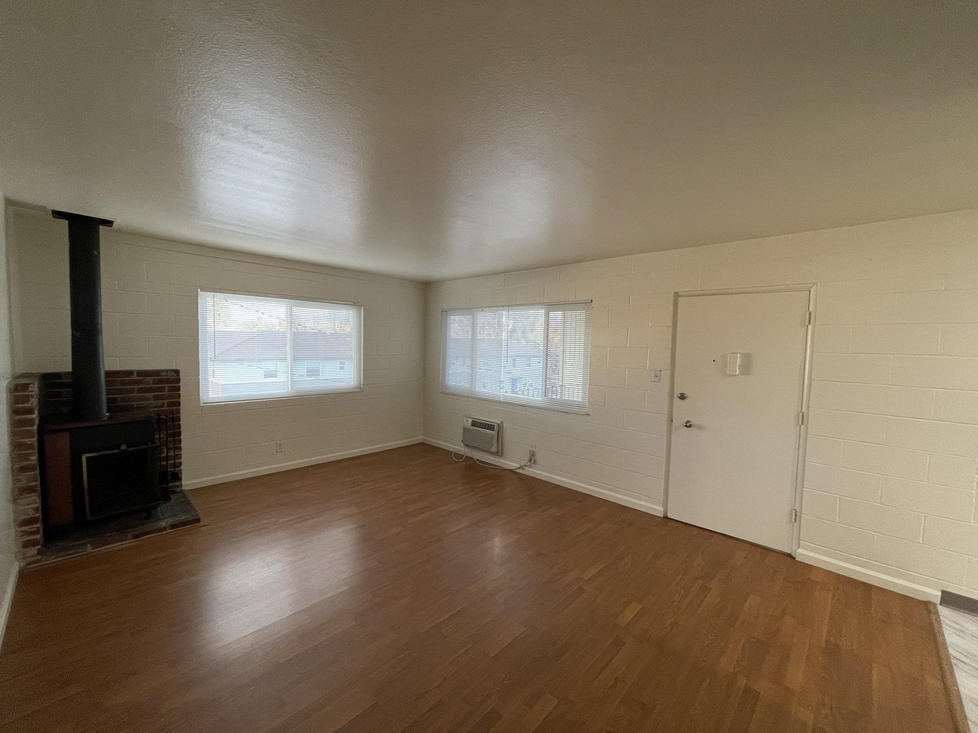 Updated studio kitchen with grey flooring, white cabinets, grey countertops, black microwave, white two electric burner stove, and white refrigerator.