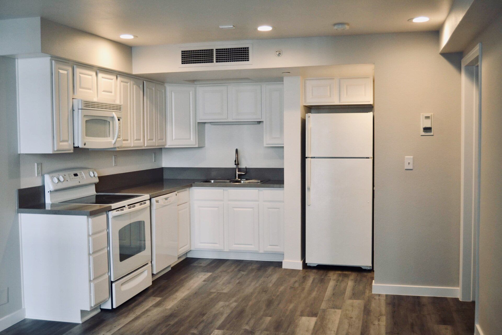 Updated kitchen with grey flooring, white cabinets, grey countertops, white microwave, white stove, and white refrigerator.