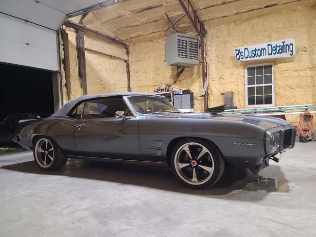 Gray classic convertible Pontiac Firebird inside a garage, next to a window.