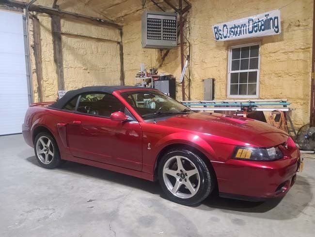Red convertible Mustang in a garage, with the top down, next to a window.