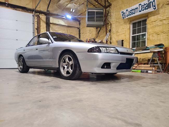 Silver Nissan Skyline R32 coupe in a garage with tools and the sign 