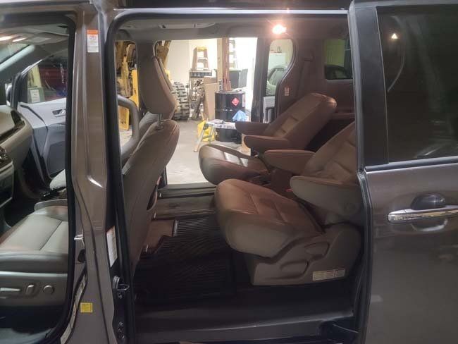 Inside view of a minivan with two rows of seats, brown interior and the sliding door open.