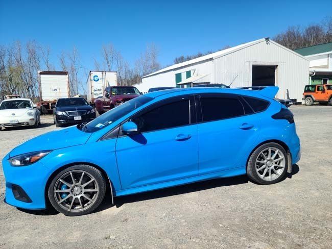 Bright blue Ford Focus RS parked on a sunny day near a white building and other vehicles.