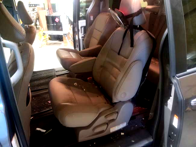 Interior view of a vehicle with gray leather seats; debris scattered on the seats and floor, suggesting an accident.