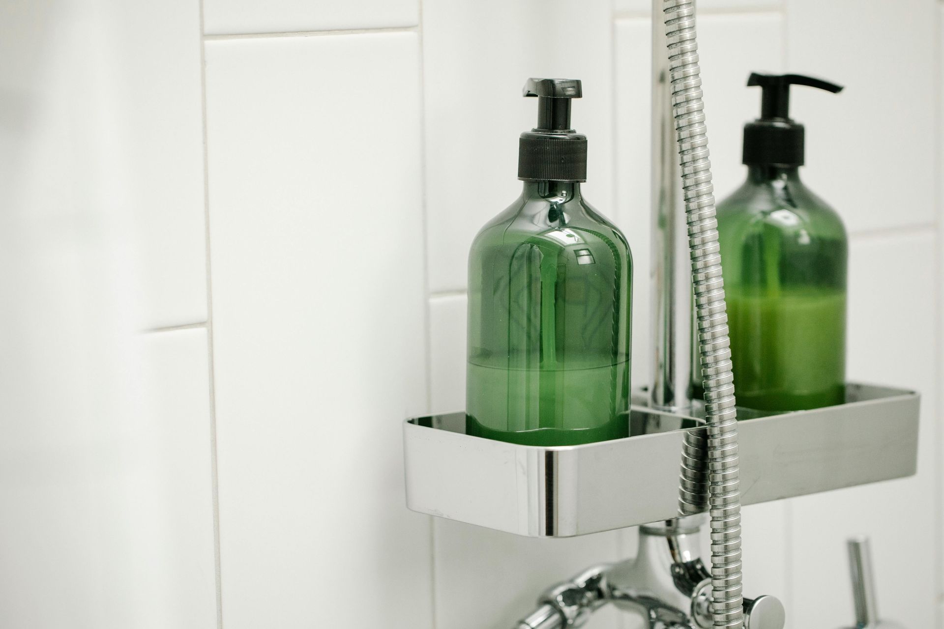 Two green bottles of soap are sitting on a shelf next to a shower head.