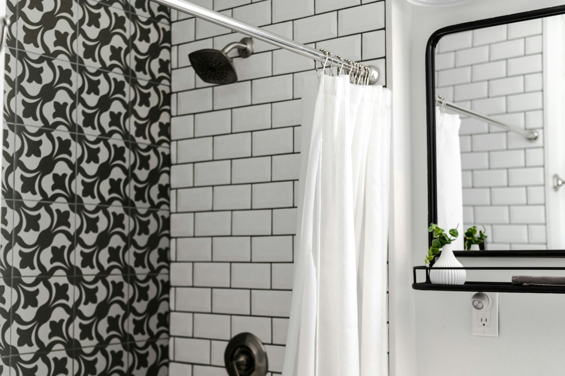 A bathroom with white tiles, a shower curtain, a mirror, and a vase.