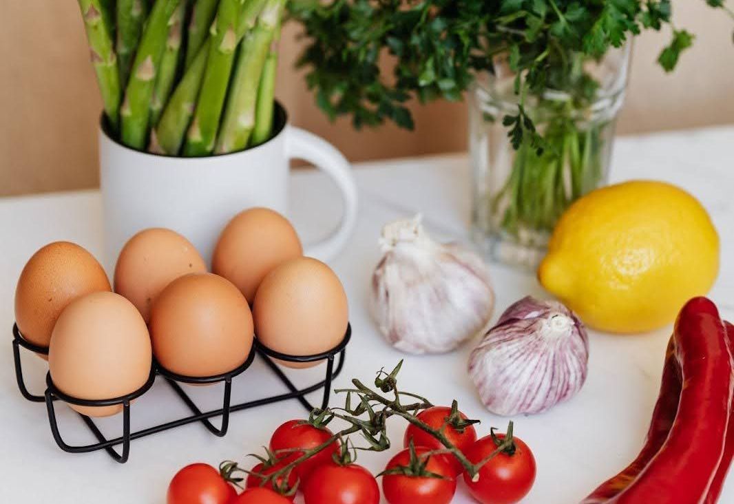 Eggs, tomatoes, onions, lemon, pepper, asparagus, herbs on a countertop.