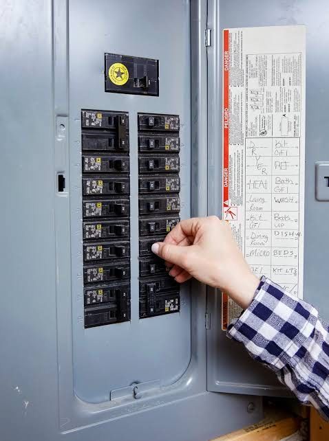 Electrical panel with circuit breakers and wires inside a gray cabinet.