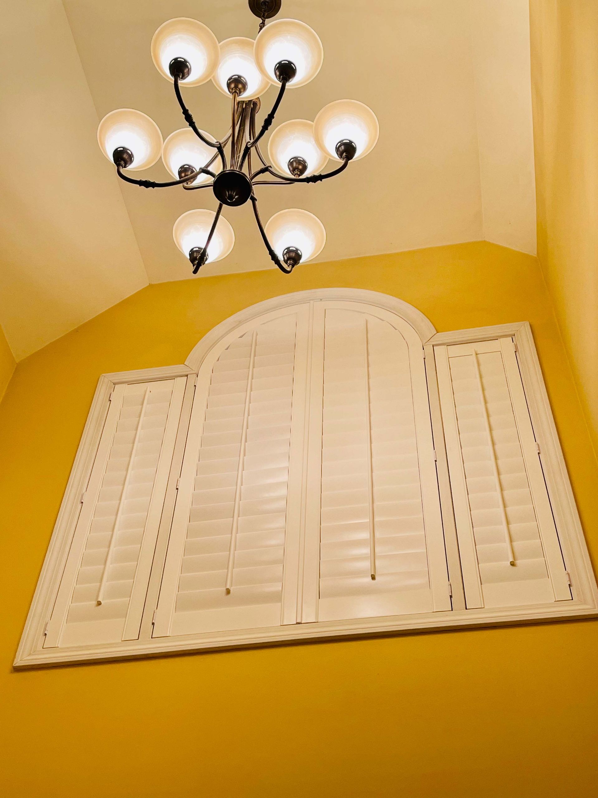 A chandelier is hanging from the ceiling above a window with shutters