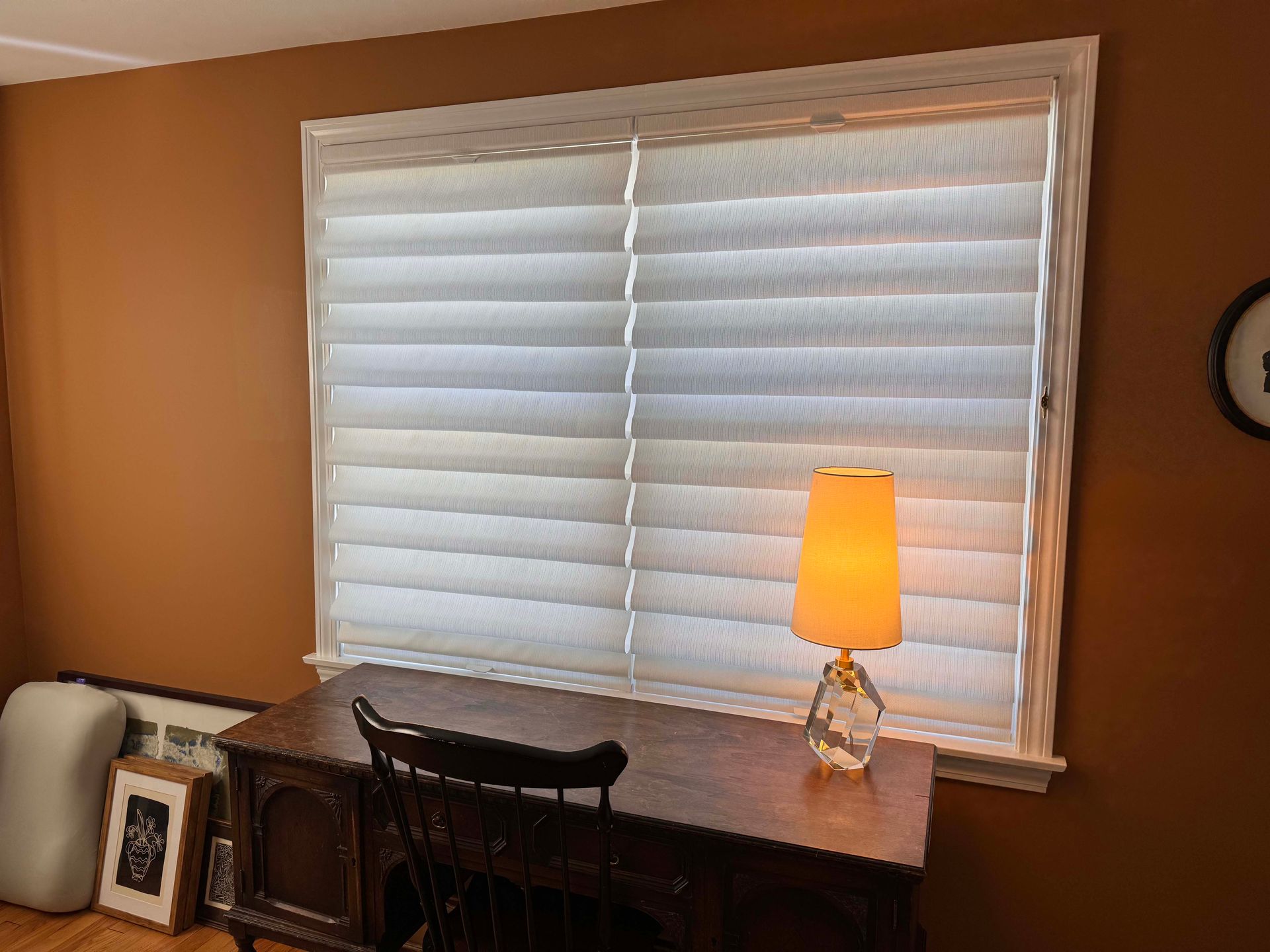 There is a lamp on the desk in front of the window.