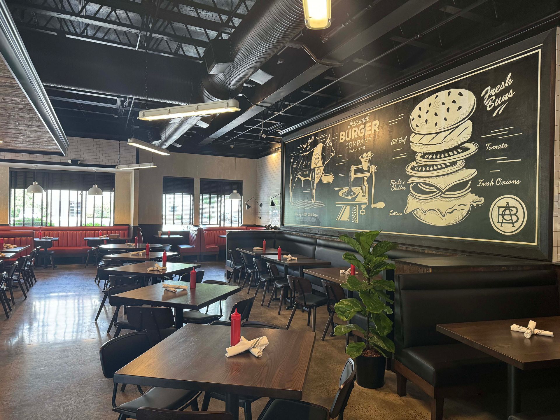 A restaurant with tables and chairs and a large chalkboard on the wall.