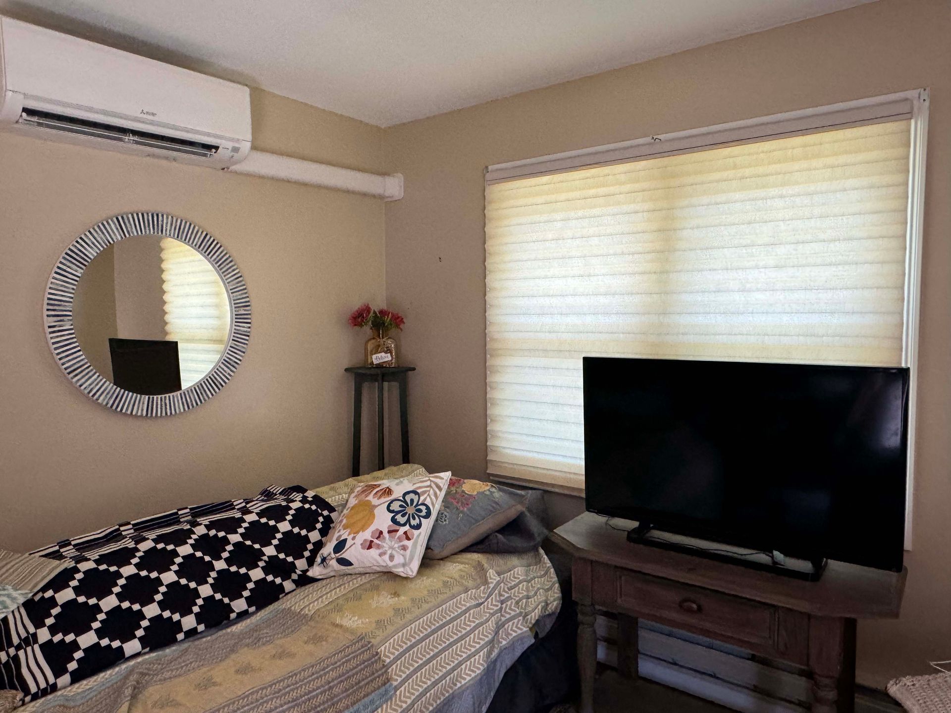 A bedroom with a bed , television , mirror and air conditioner.