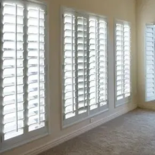 A room with lots of windows and white shutters on them.