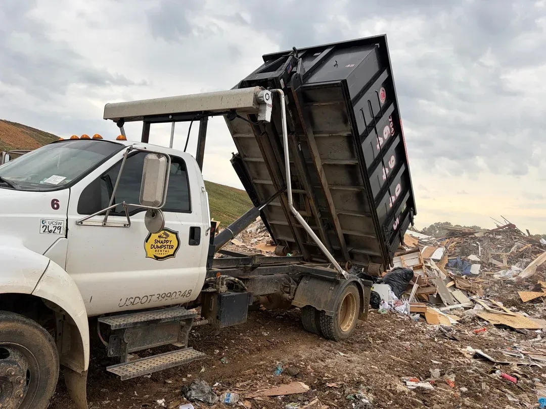 White dump truck unloading debris at a landfill under a cloudy sky