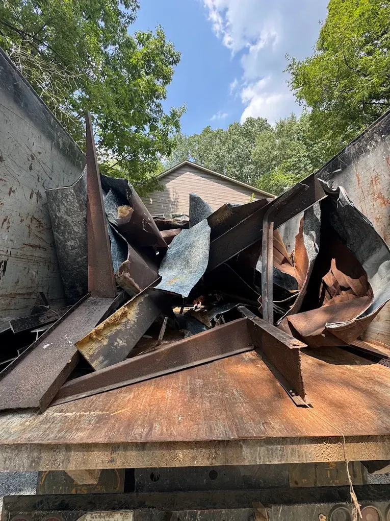 Damaged metal dumpster with bent panels and rust under a leafy blue sky