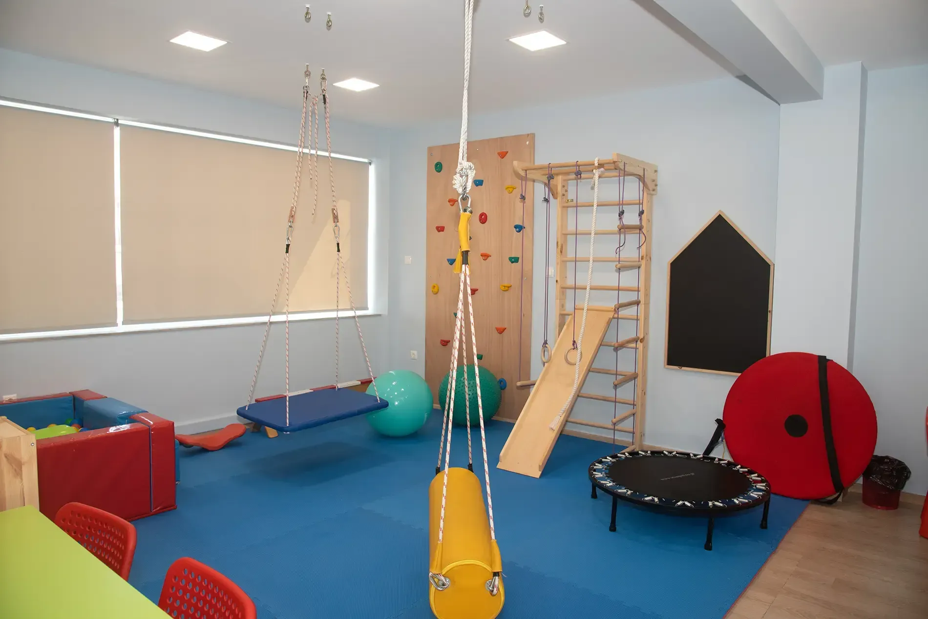Ένα γυμναστήριο με τοίχο αναρρίχησης, κούνιες, τραμπολίνο και πίνακα κιμωλίας.