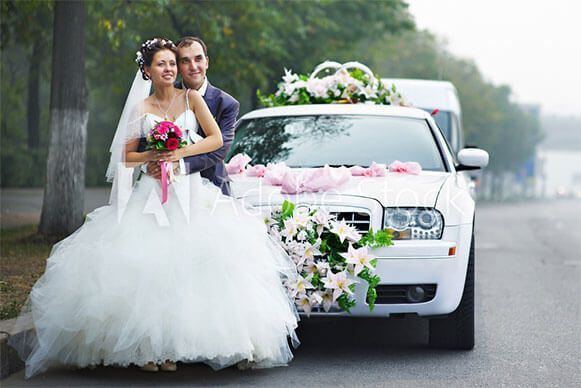 A bride and groom are posing for a picture in front of a decorated wedding car.