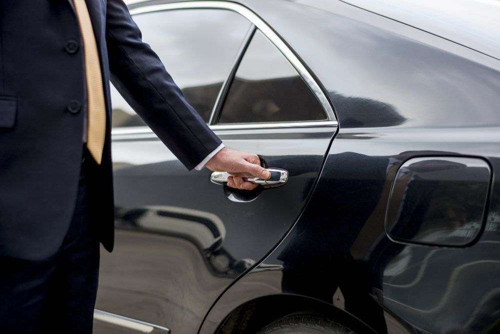 A man in a suit and tie is opening the door of a car