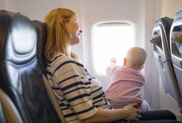 A pregnant woman is sitting on an airplane holding a baby.