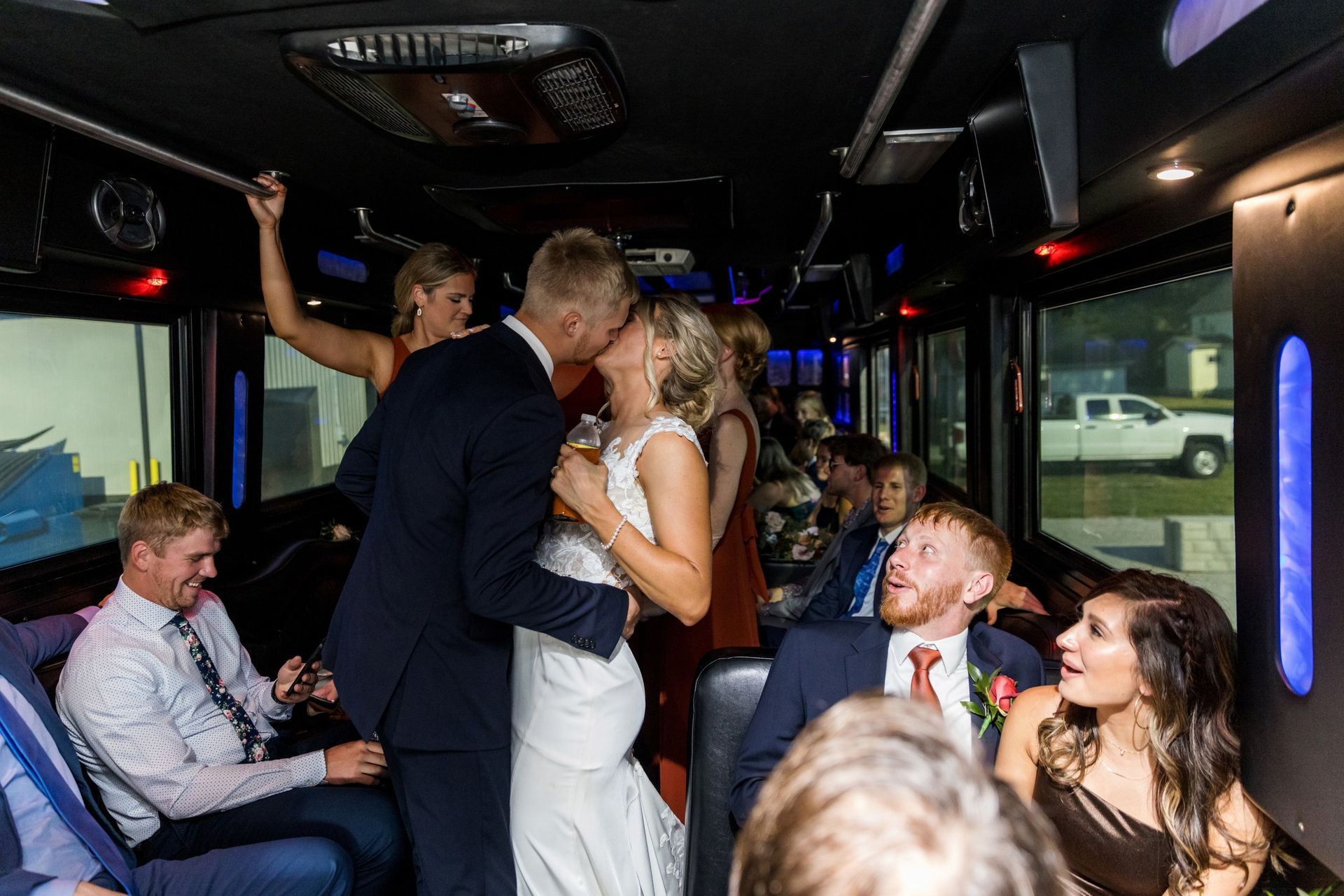 Bride and groom in a limousine, smiling, holding hands, she in a white gown, he in a black suit.