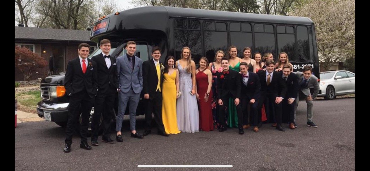 Prom picture: Eight young adults in formal wear, posing outdoors. Dresses are red, blue, white, and pink. Couples smiling.