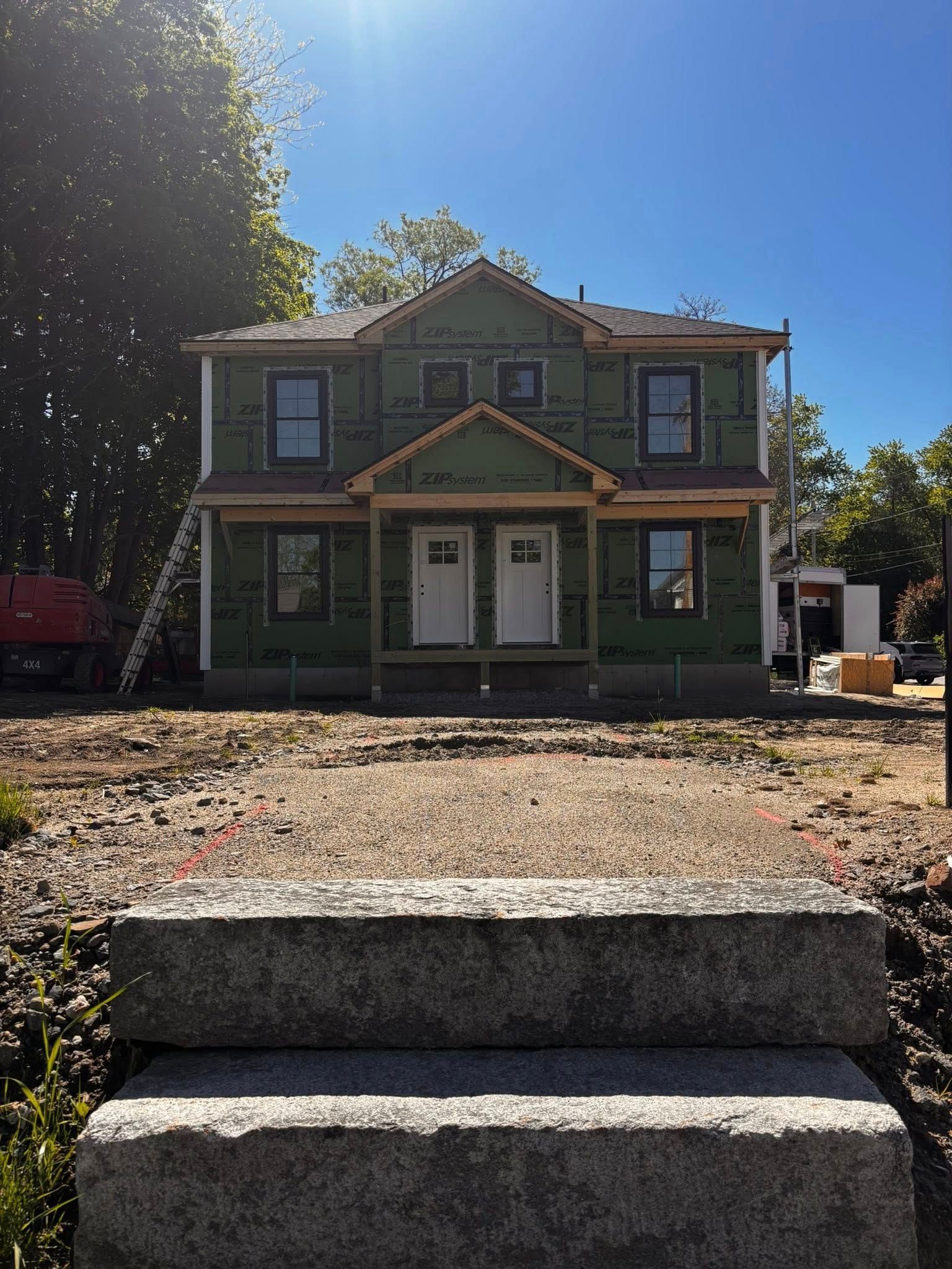 Green two-story house under construction with front porch and stone steps in bright sunlight