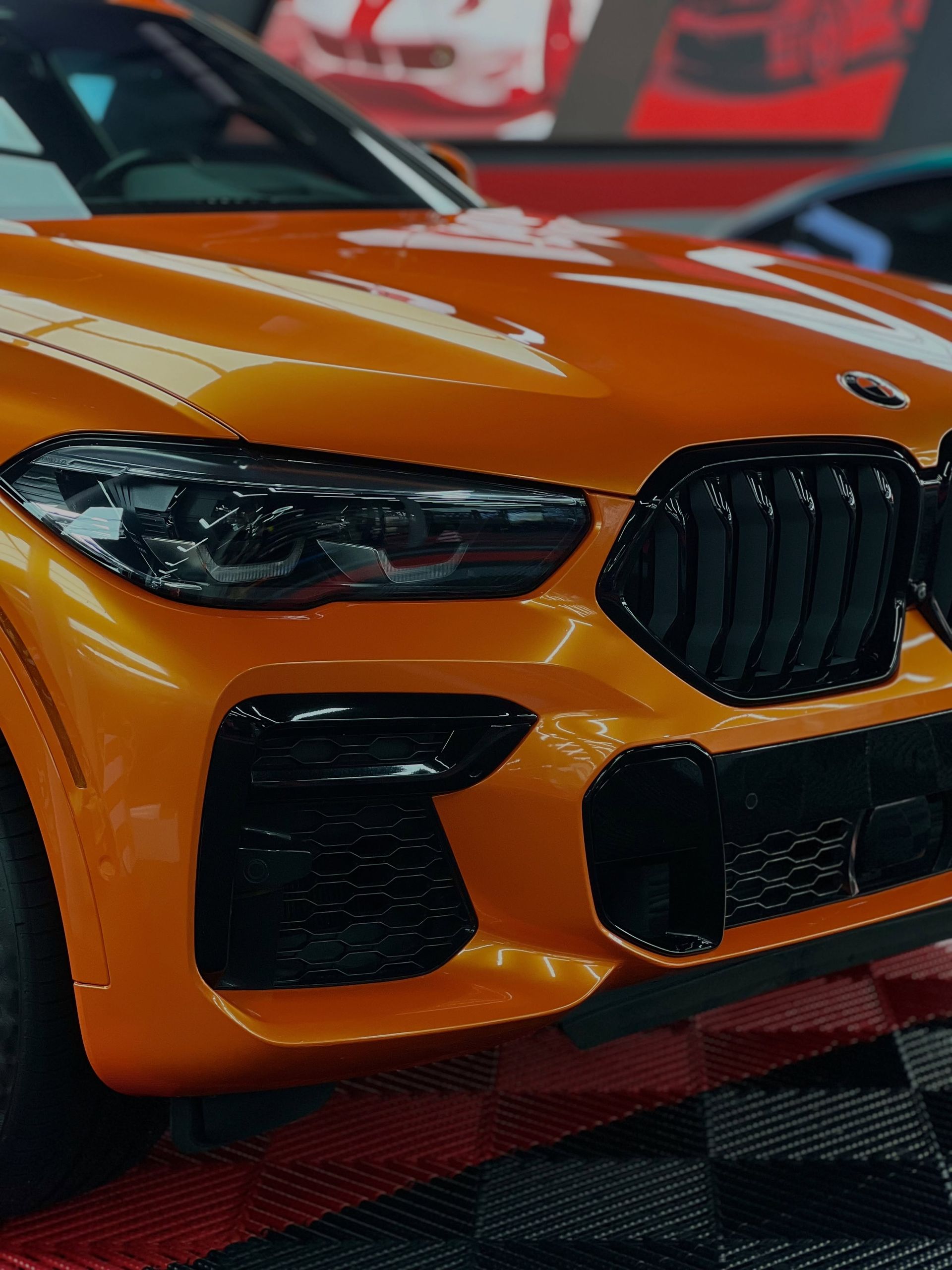 Orange sports car front grille and headlights, close-up on a checkered display floor.