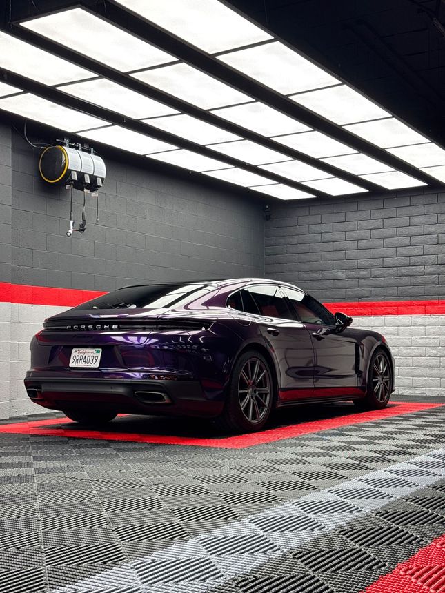 Black sports car in a modern showroom with dark walls and patterned floor, lit by overhead panels