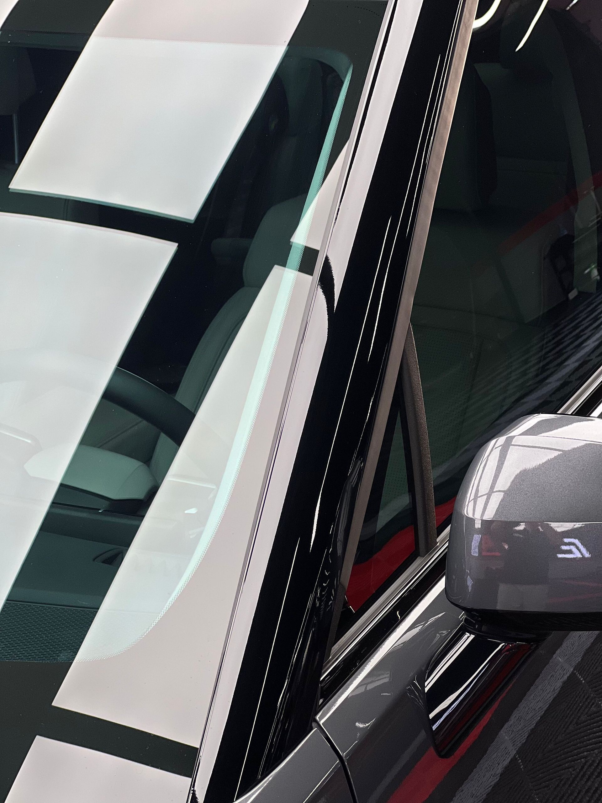 Close-up of a black car windshield and side mirror with a white reflective strip on the glass