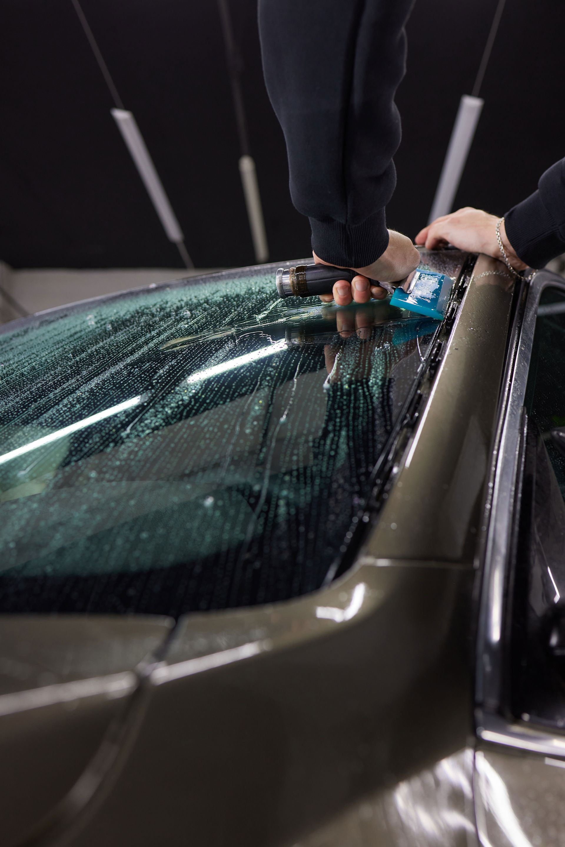 Person scraping ice off a car windshield with a tool at a car wash at night