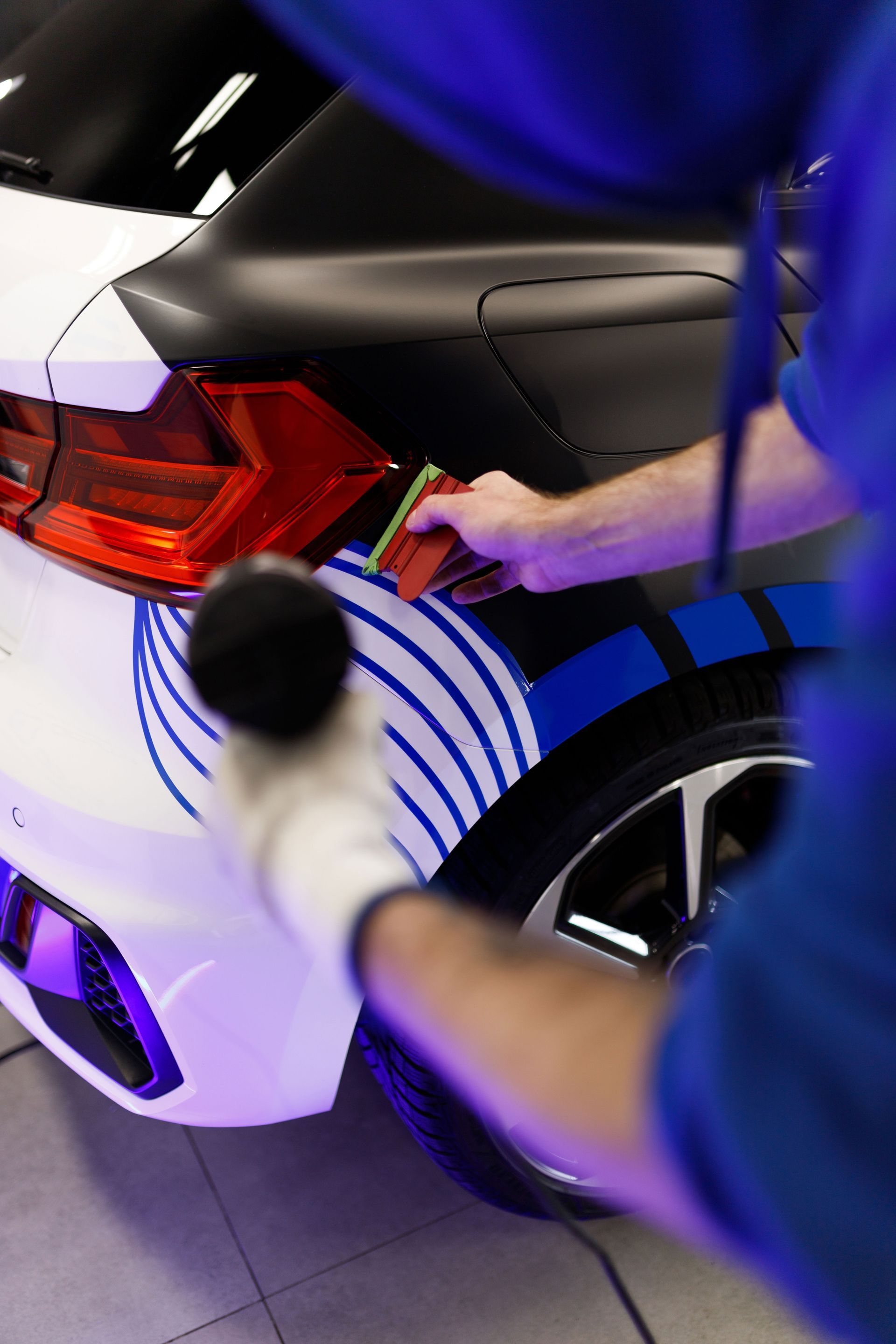 Person cleaning the rear light of a white car with a cloth and spray bottle at night