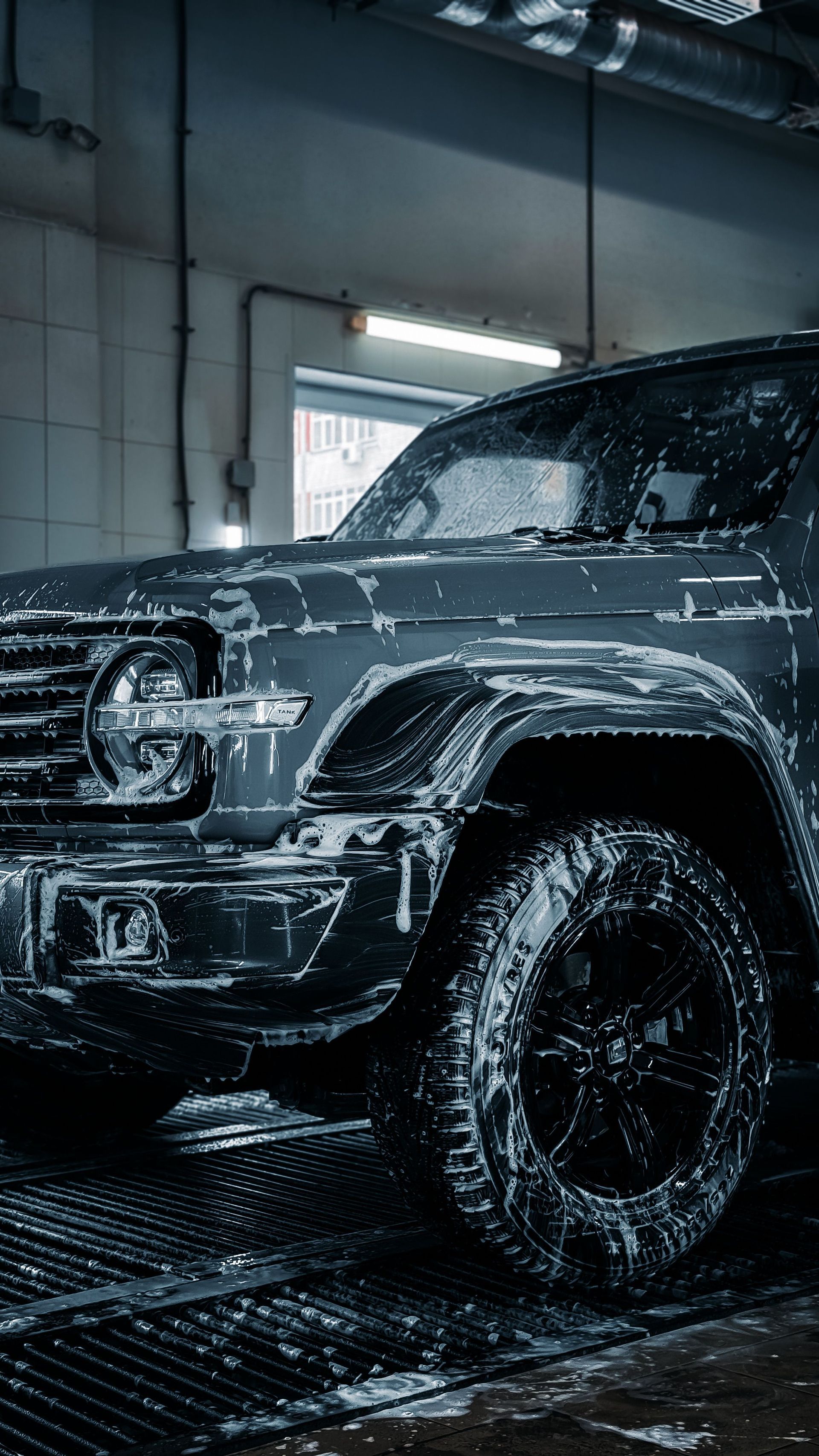 Black SUV being washed in a car wash bay, covered in soap suds and water spray