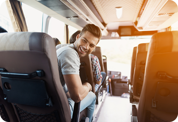 Homem sorri sentado no banco do ônibus, olhando para a câmera. Interior iluminado pela luz do sol.