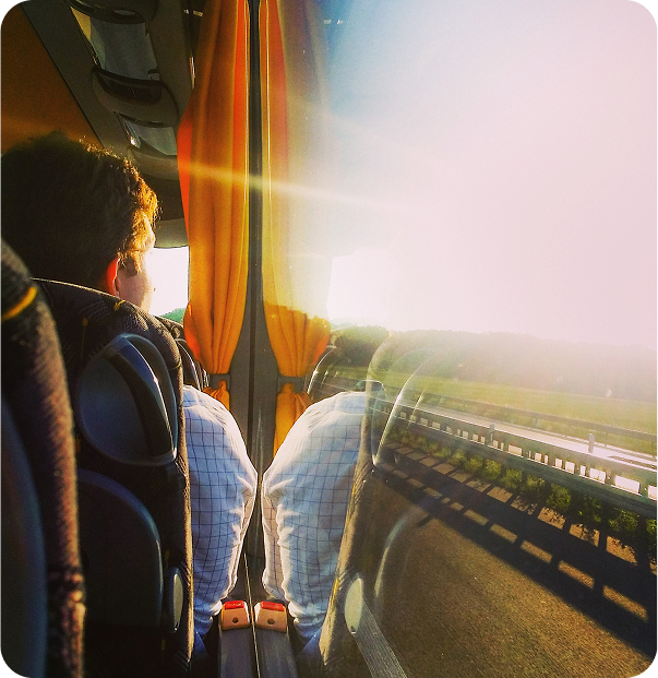 Pessoa olhando pela janela do ônibus, luz do sol forte, vista da rodovia.