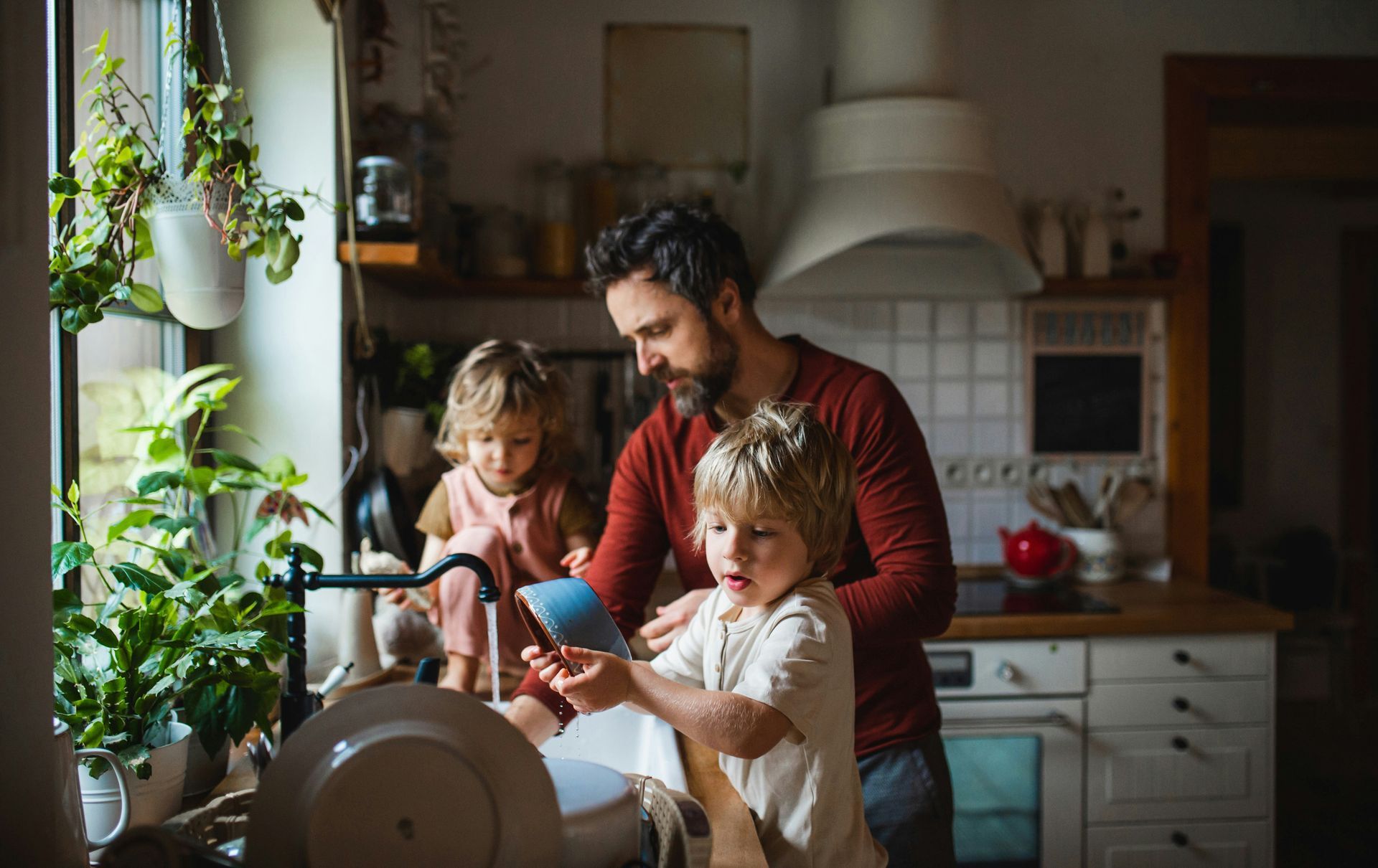 A man and two children are washing dishes in a kitchen.