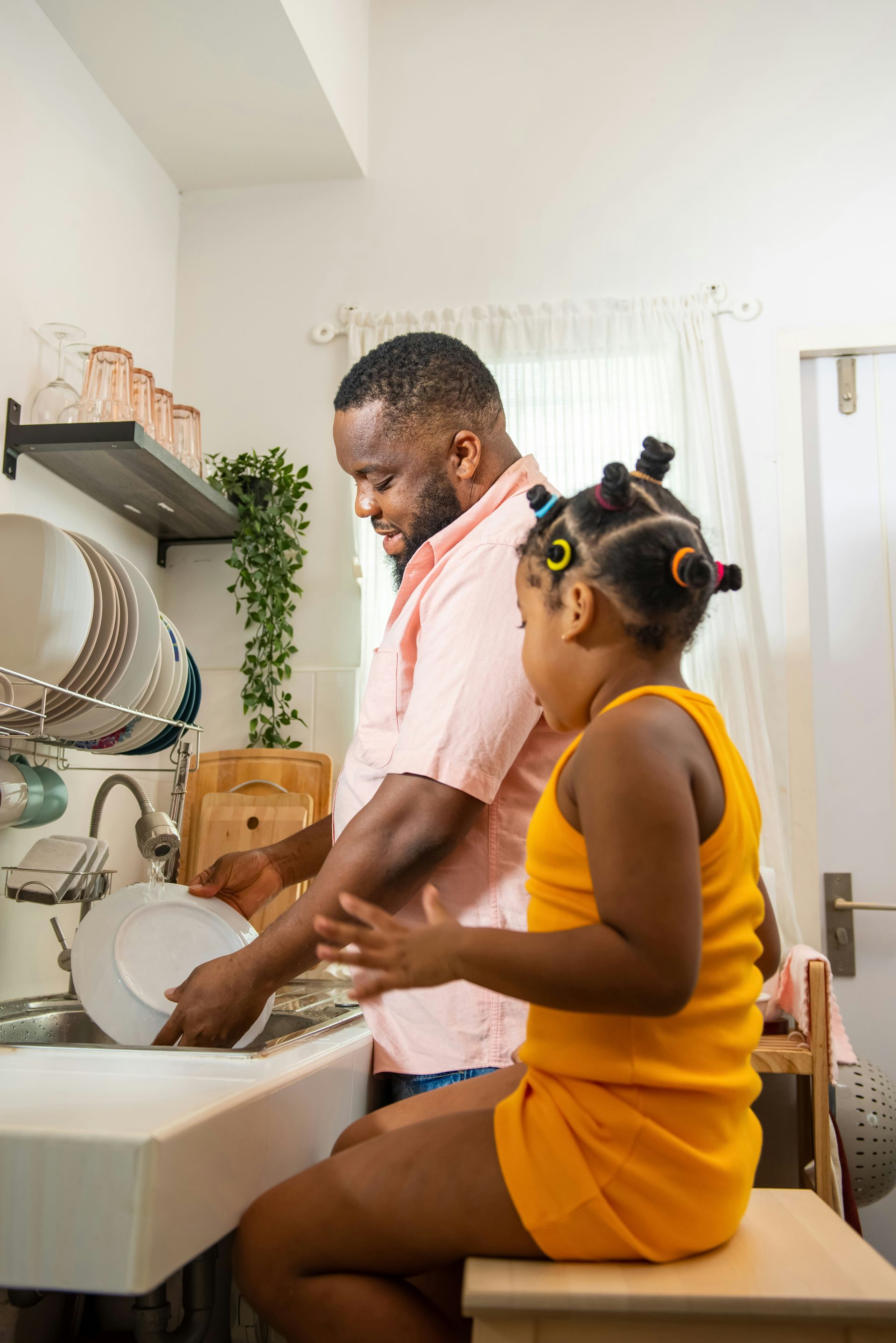 A man and a little girl are washing dishes in a kitchen sink.