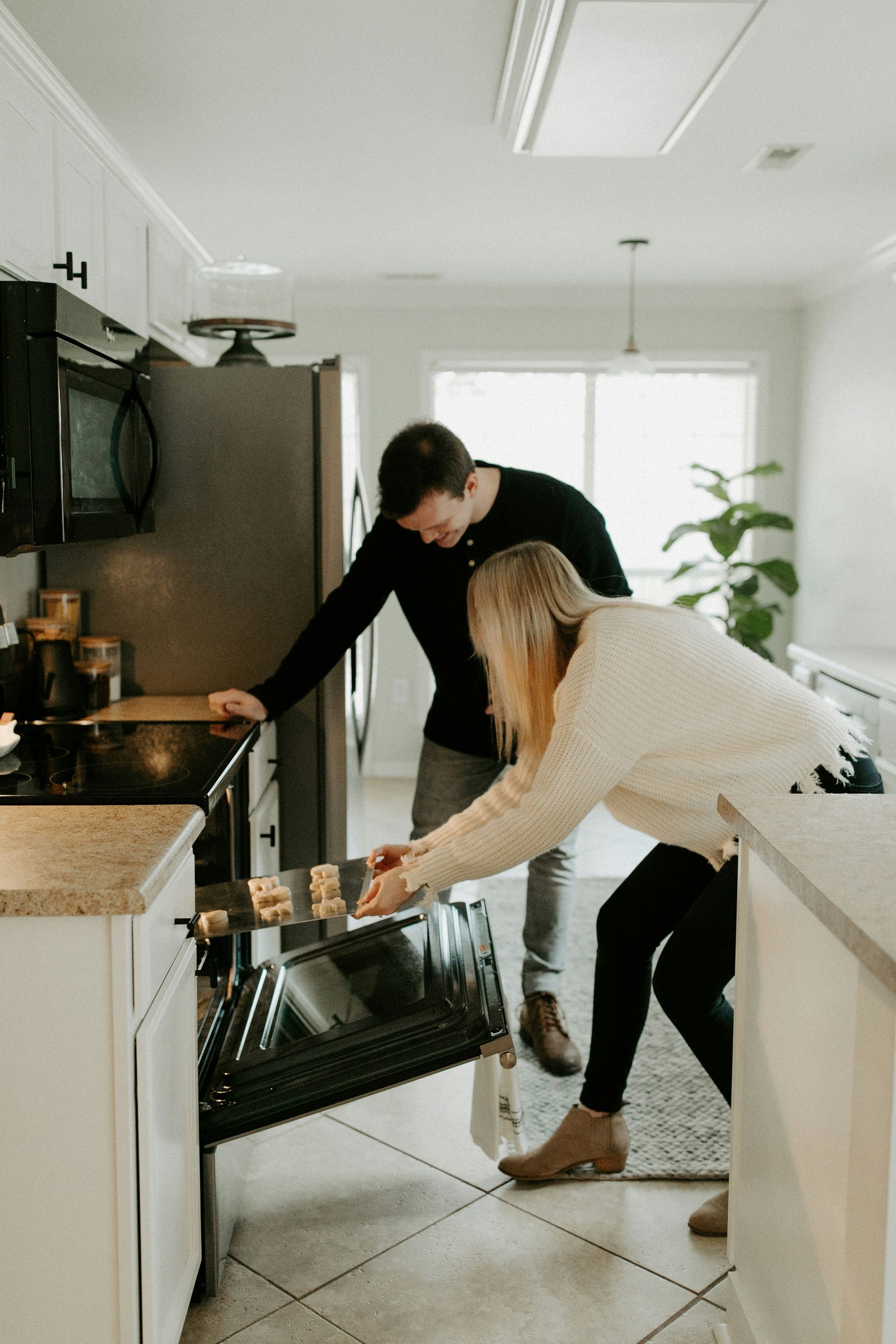 A man and a woman are standing in a kitchen looking into an oven.